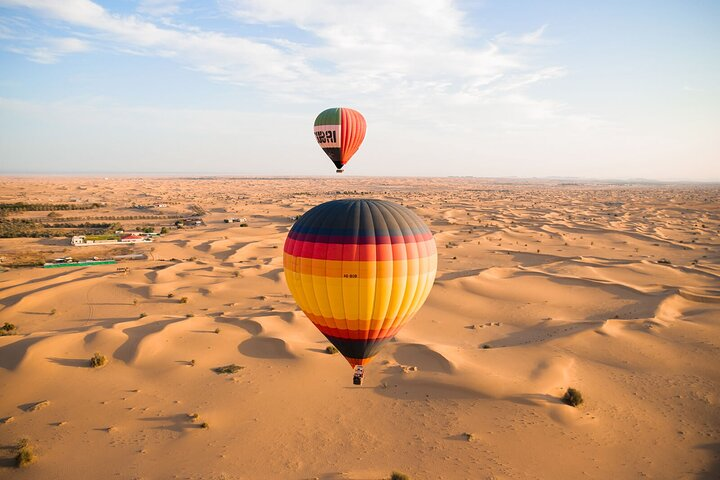 Experience breathtaking desert sunrises from a hot air balloon surrounded by vast golden dunes setting the stage for unforgettable adventures like dune bashing and camel riding.